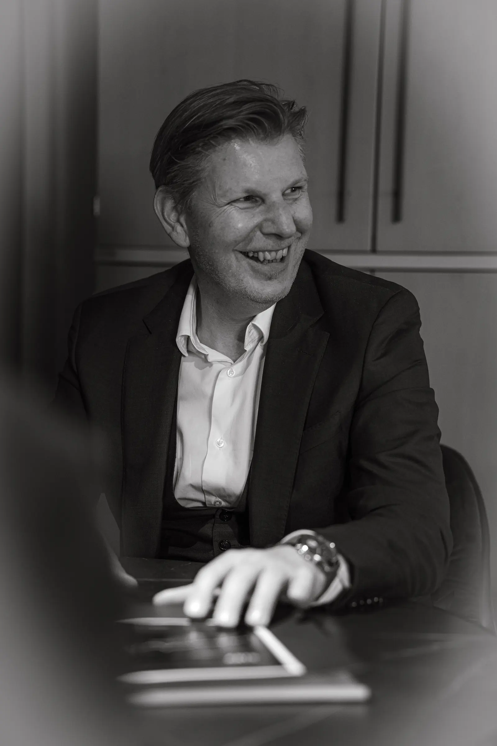Porträt Helmut Hemmelmeir, lachend am Besprechungstisch, schwarzweiß